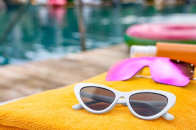 Beach towel and sunglasses near outdoor swimming pool at luxury resort, closeup. Space for text