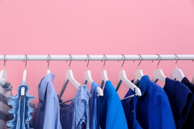 Rack with bright clothes on color background