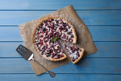 Delicious cut currant pie and spatula on blue wooden table, flat lay
