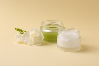 Moisturizing cream in open jars and freesia flower on beige background. Body care products