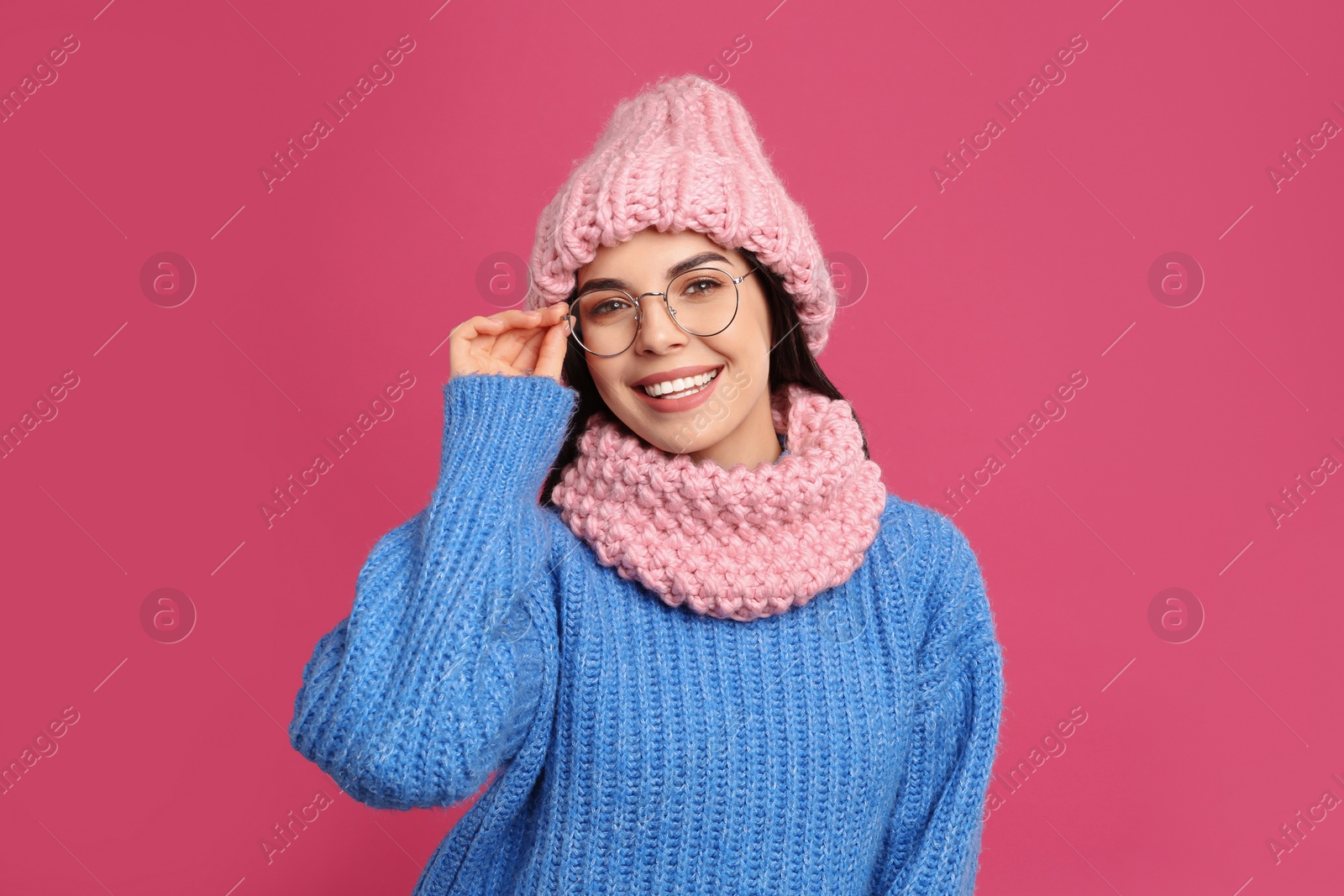 Photo of Young woman wearing warm sweater, snood and hat on crimson background. Winter season