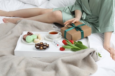 Photo of Tasty breakfast served in bed. Woman with gift box, desserts, tea, flowers and I Love You card at home, closeup