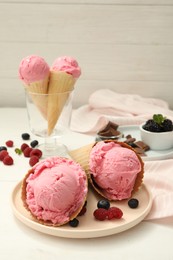 Delicious pink ice cream in wafer cones with berries on white wooden table