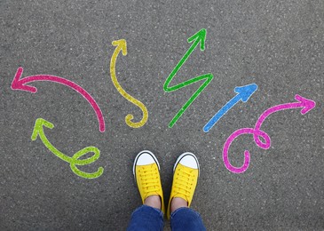 Image of Choosing future profession. Girl standing in front of drawn signs on asphalt, top view. Arrows pointing in different directions symbolizing diversity of opportunities
