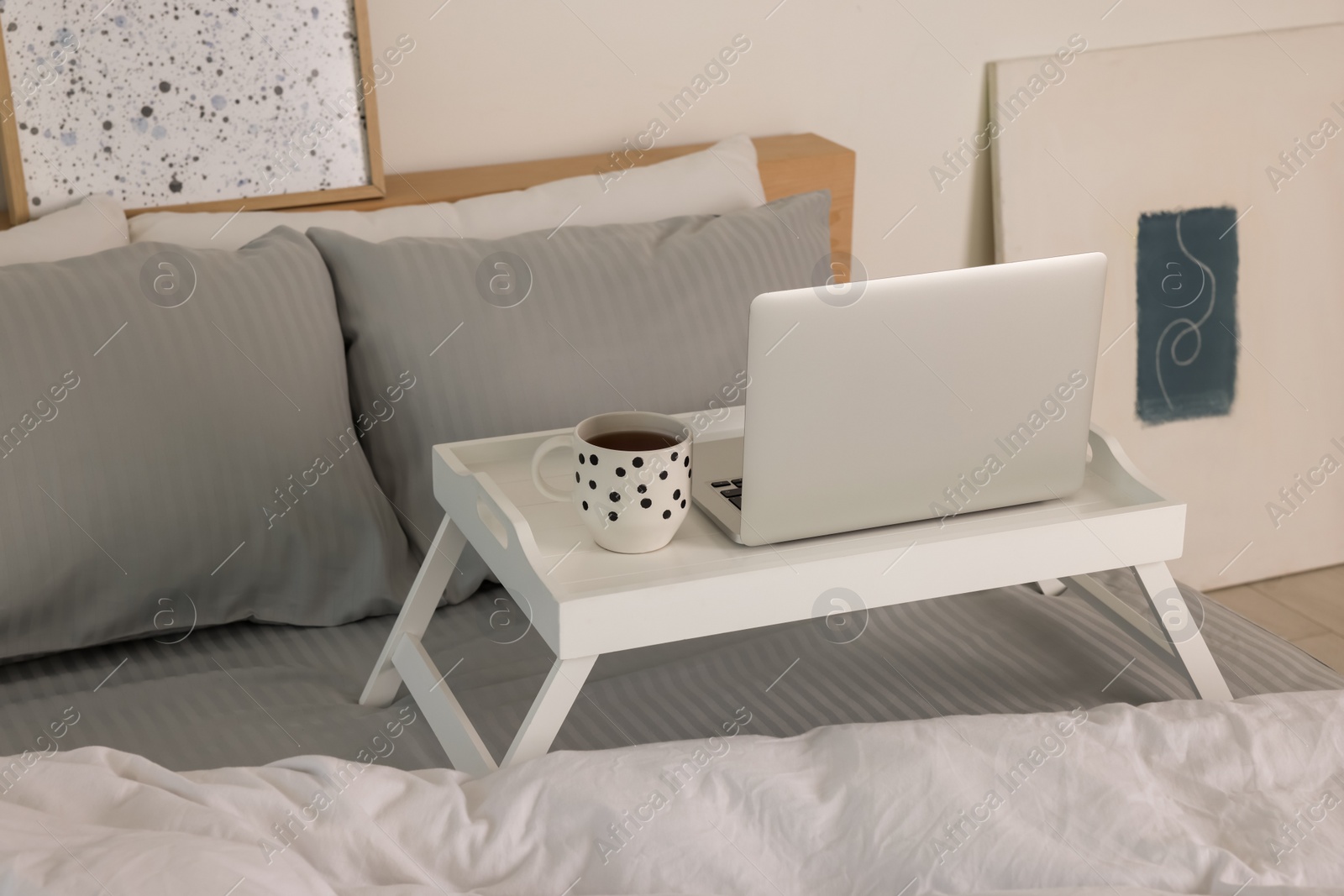 Photo of White tray table with laptop and cup of drink on bed indoors