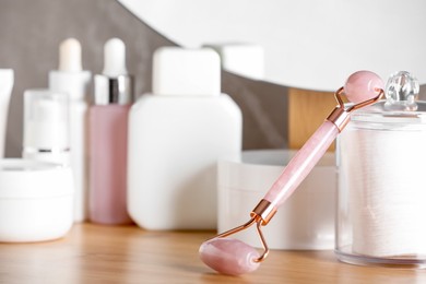 Photo of Natural face roller and cosmetic products on wooden dressing table, closeup. Space for text