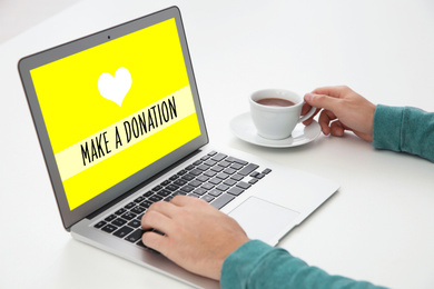 Image of Donations concept. Man with laptop and cup of coffee at white table, closeup