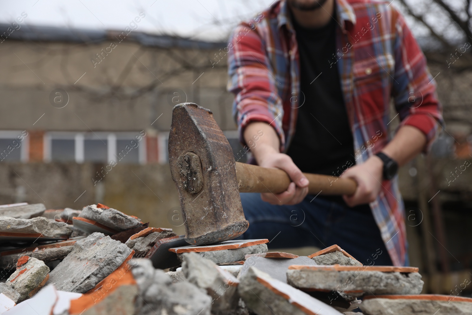 Photo of Man breaking bricks with sledgehammer outdoors, selective focus