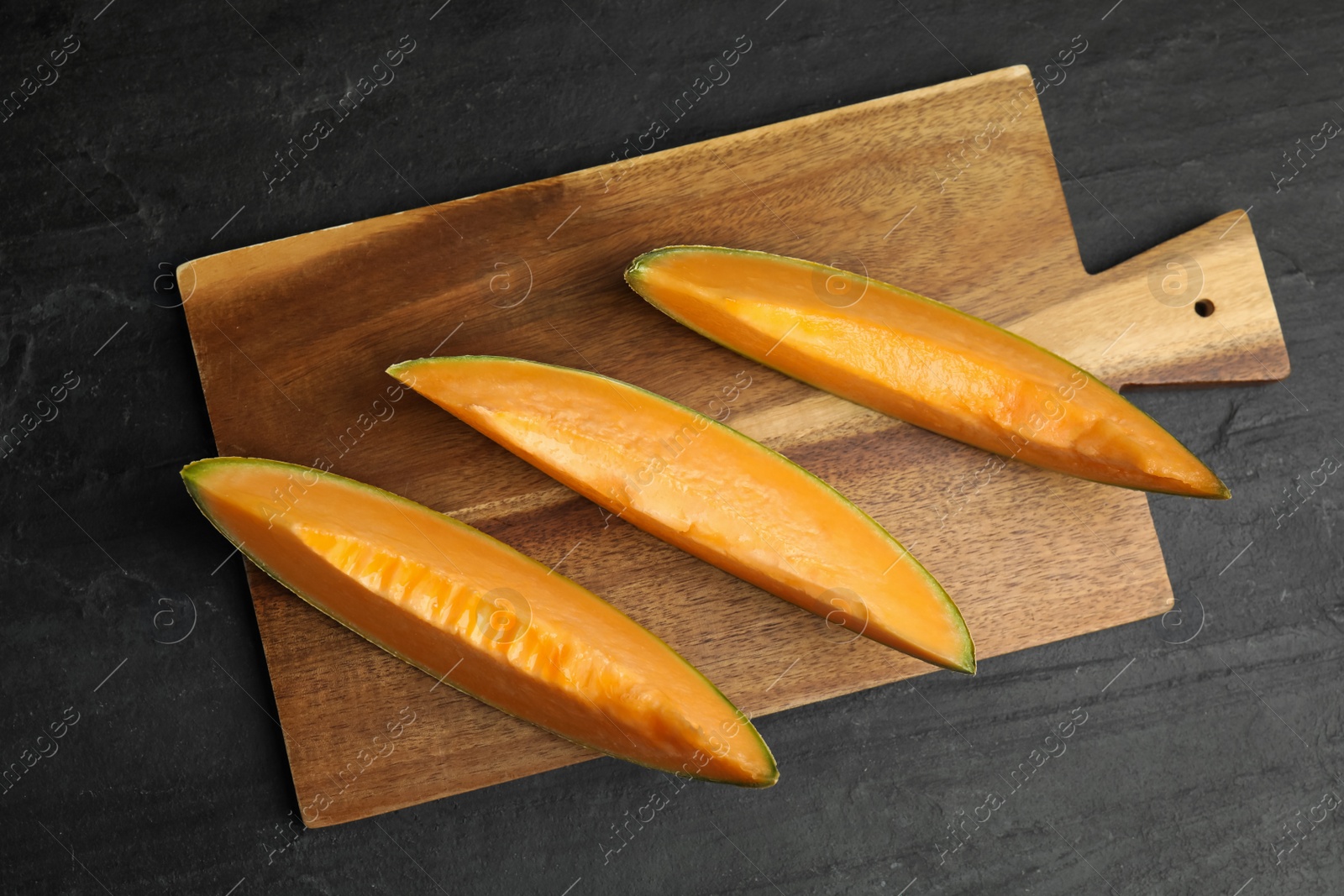 Photo of Slices of tasty fresh melon on black slate table, top view