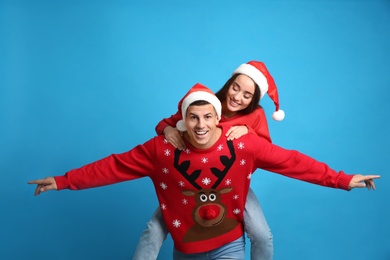Photo of Couple in Christmas sweaters and Santa hats on blue background