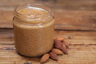 Photo of Tasty nut paste in jar and almonds on wooden table, closeup. Space for text