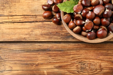 Photo of Fresh sweet edible chestnuts on wooden table, flat lay. Space for text