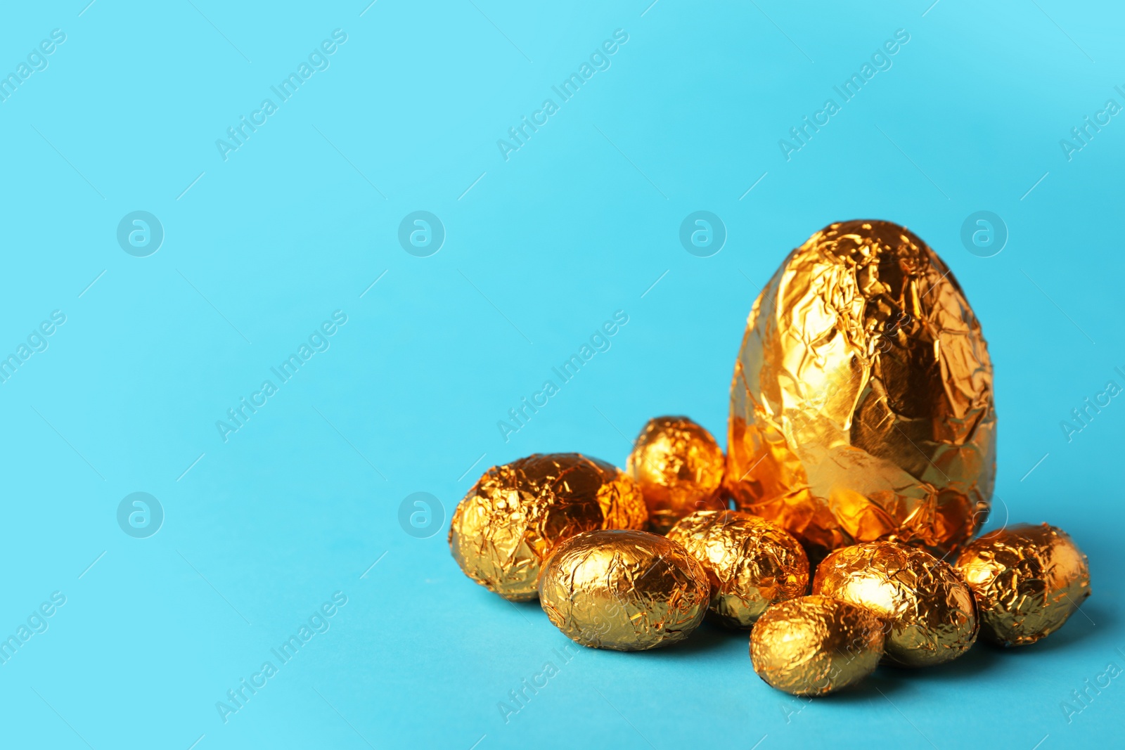 Photo of Chocolate eggs wrapped in golden foil on light blue background. Space for text