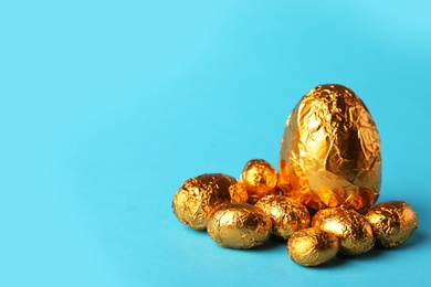 Chocolate eggs wrapped in golden foil on light blue background. Space for text