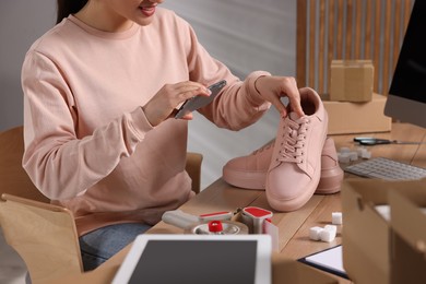 Shoes seller taking picture of pink sneakers at table in office, closeup. Online store