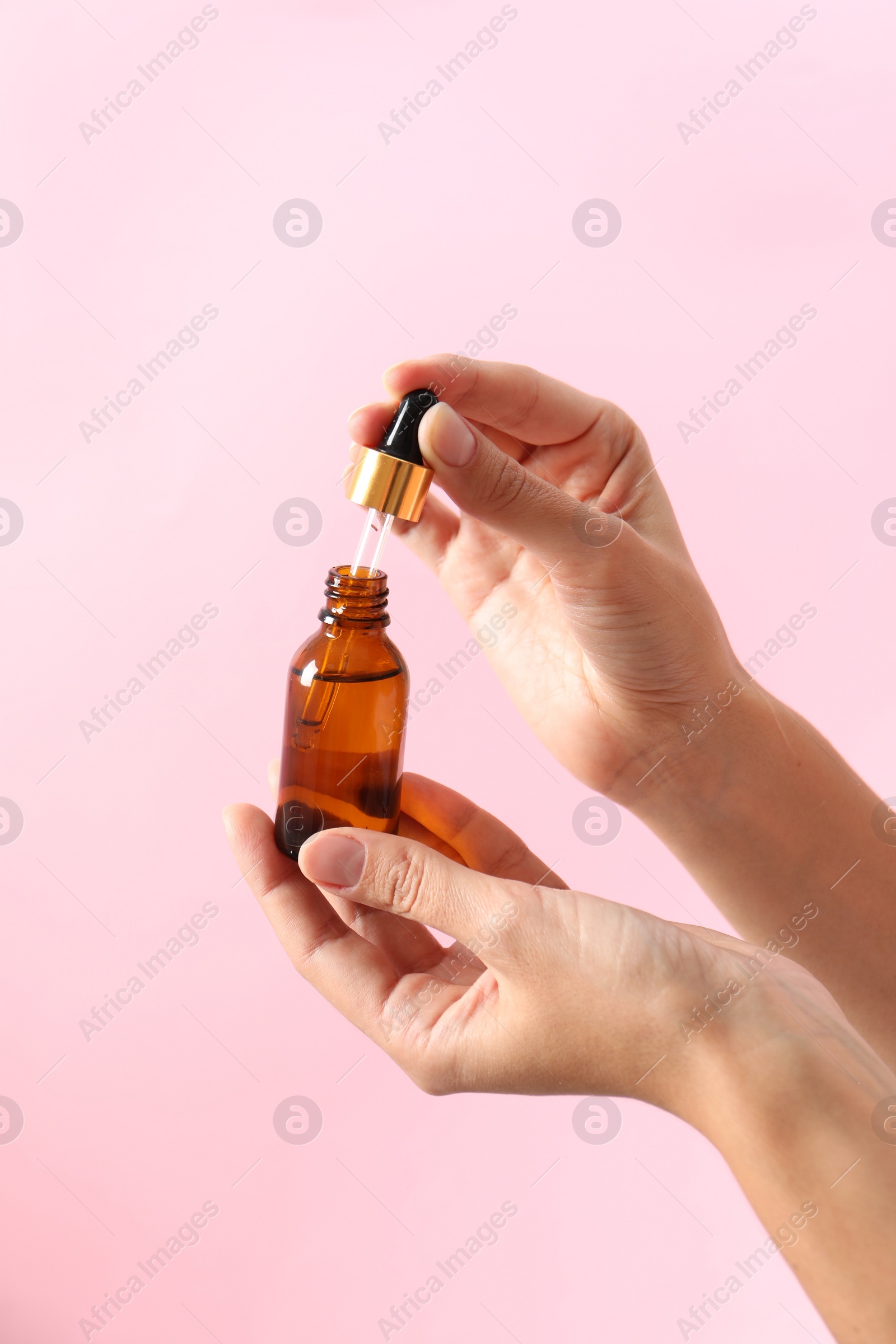 Photo of Woman with bottle of cosmetic serum and dropper on pink background, closeup