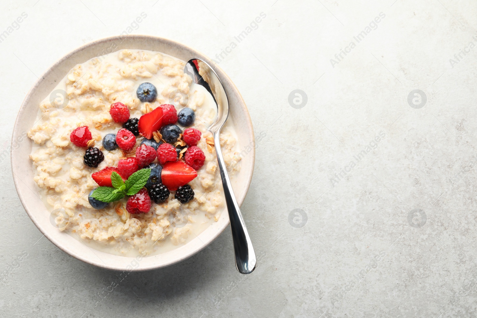 Photo of Bowl of oatmeal porridge served with berries on light grey table, top view. Space for text