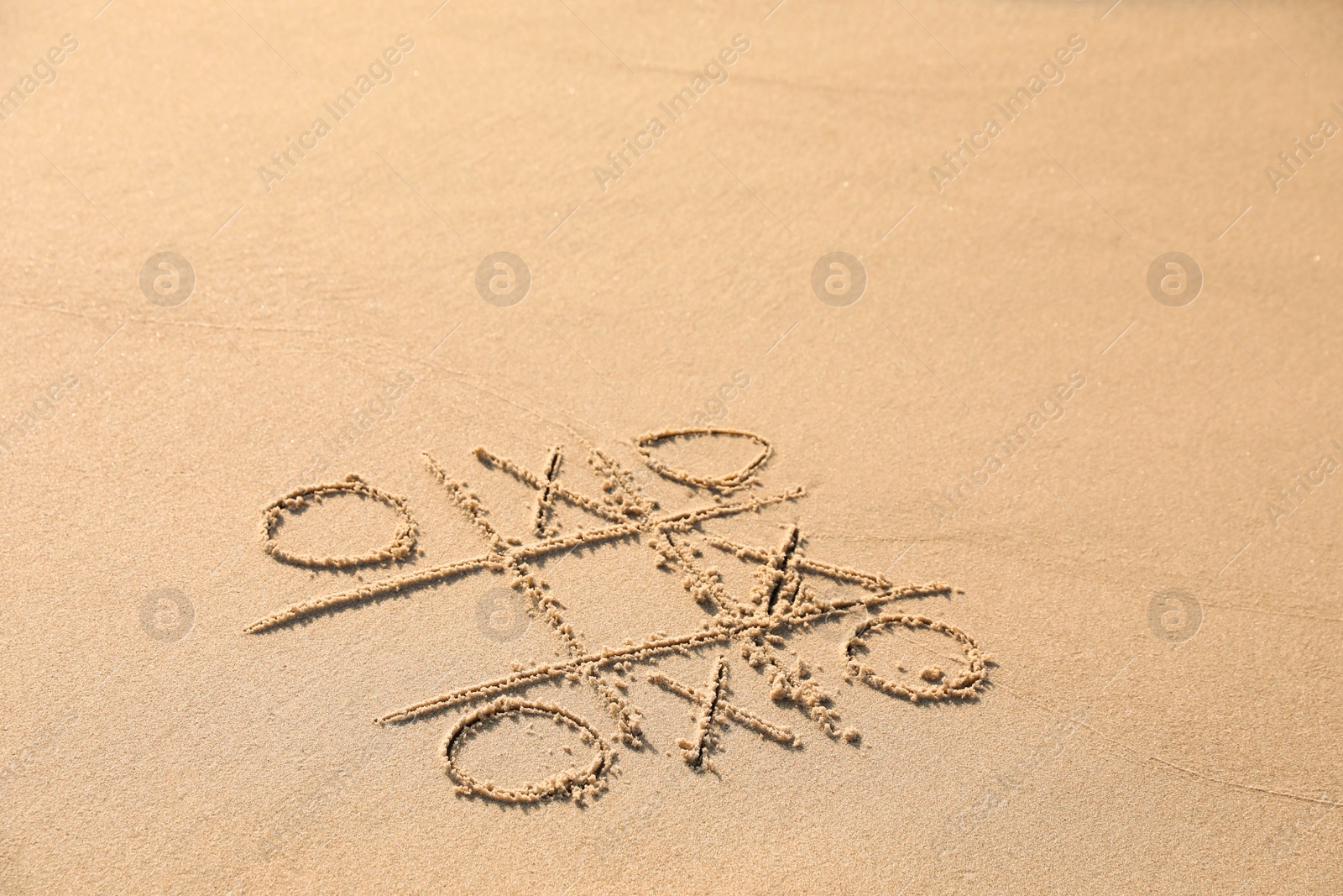 Photo of Tic tac toe game drawn on sandy beach. Space for text