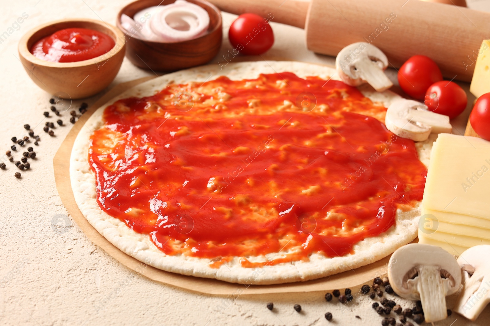 Photo of Pizza base smeared with tomato sauce, peppercorns and products on light textured table, closeup