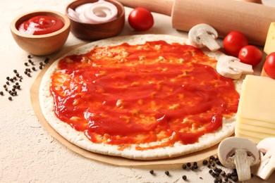 Pizza base smeared with tomato sauce, peppercorns and products on light textured table, closeup