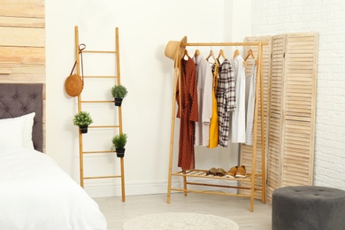 Wooden rack with clothes in modern bedroom interior