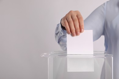 Photo of Woman putting her vote into ballot box on light grey background, closeup. Space for text