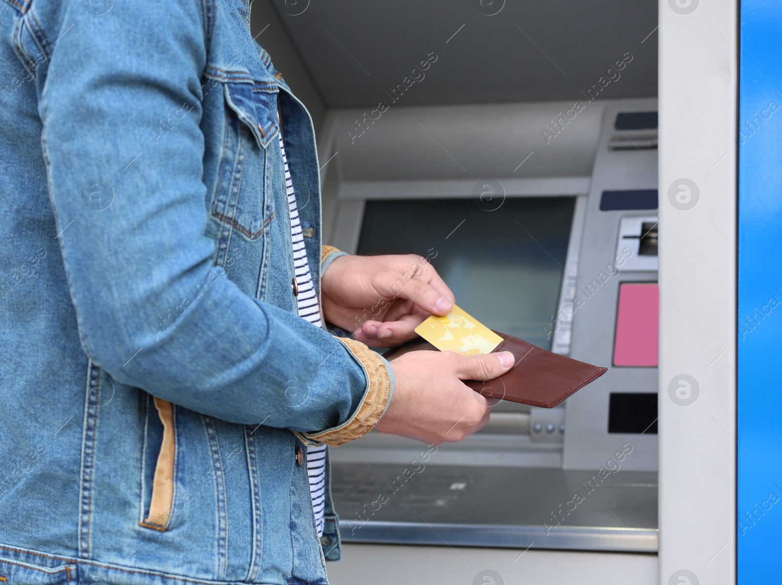 Photo of Young man with credit card near cash machine outdoors, closeup