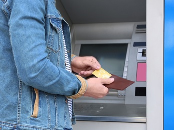 Young man with credit card near cash machine outdoors, closeup