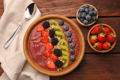 Photo of Bowl of delicious smoothie with fresh blueberries, strawberries, kiwi slices and blackberries on wooden table, flat lay