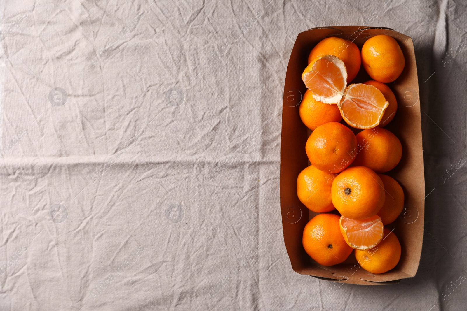 Photo of Paper box with fresh ripe tangerines on beige cloth, top view. Space for text