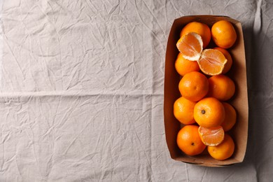Photo of Paper box with fresh ripe tangerines on beige cloth, top view. Space for text