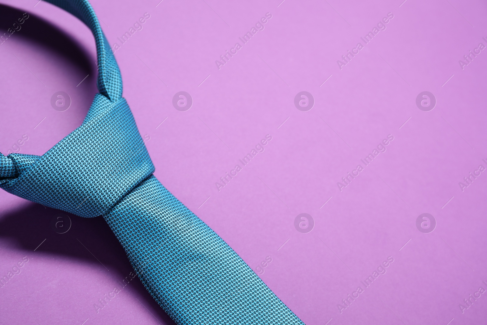 Photo of Turquoise necktie on purple background, top view. Space for text
