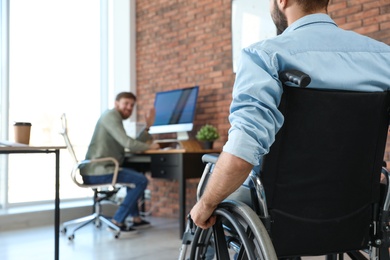Photo of Young man in wheelchair with colleague at office, closeup