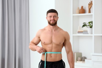 Photo of Portrait of happy athletic man measuring waist with tape at home. Weight loss concept