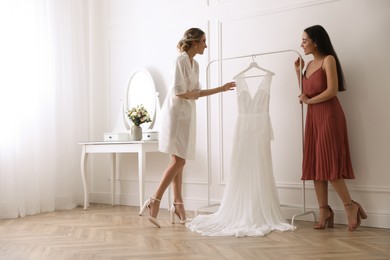 Young bride with her friend near wedding dress indoors