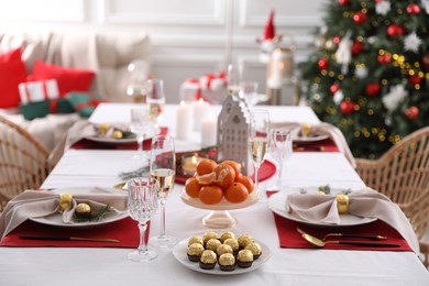 Photo of Christmas table setting with tangerines, candies and dishware indoors