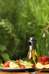 Photo of Spray bottle of cooking oil and delicious salad on wooden table against blurred background