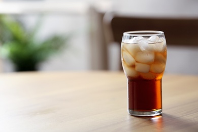 Glass of cola with ice on table against blurred background, space for text