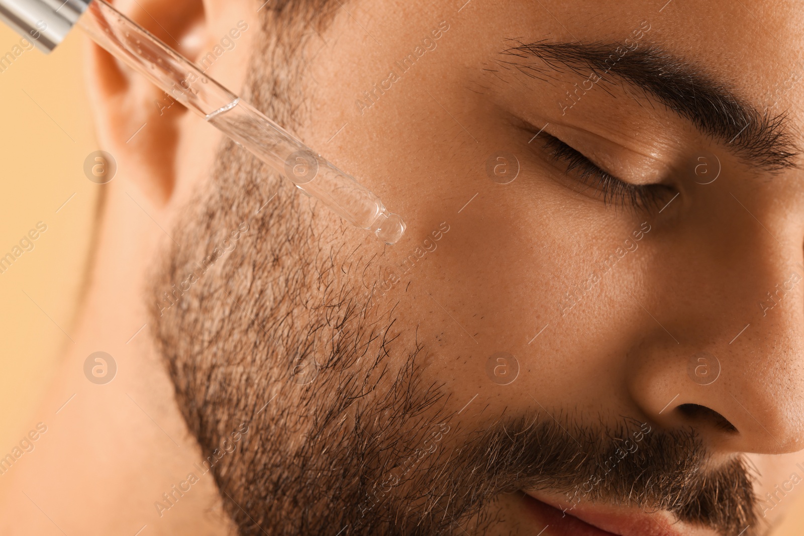 Photo of Man applying cosmetic serum onto face, closeup