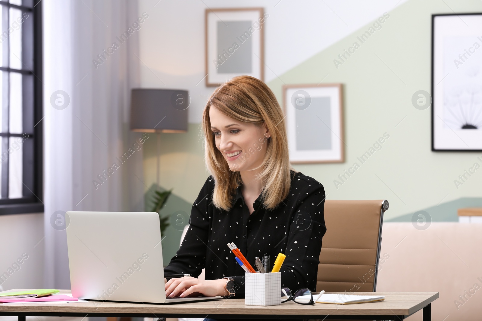 Photo of Young woman working with laptop at desk in home office