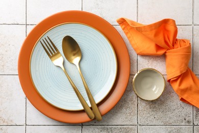 Photo of Stylish setting with cutlery, napkin and plates on light tiled table, top view