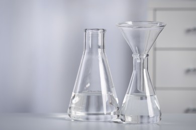 Photo of Conical flasks with transparent liquid and funnel on table in laboratory. Space for text