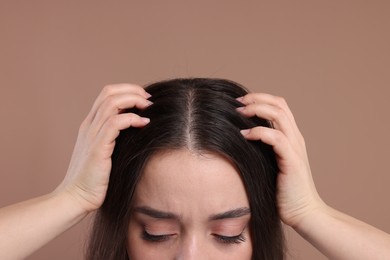 Woman examining her hair and scalp on beige background, closeup