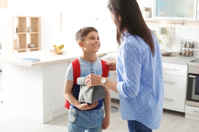 Photo of Young woman helping her little child get ready for school at home