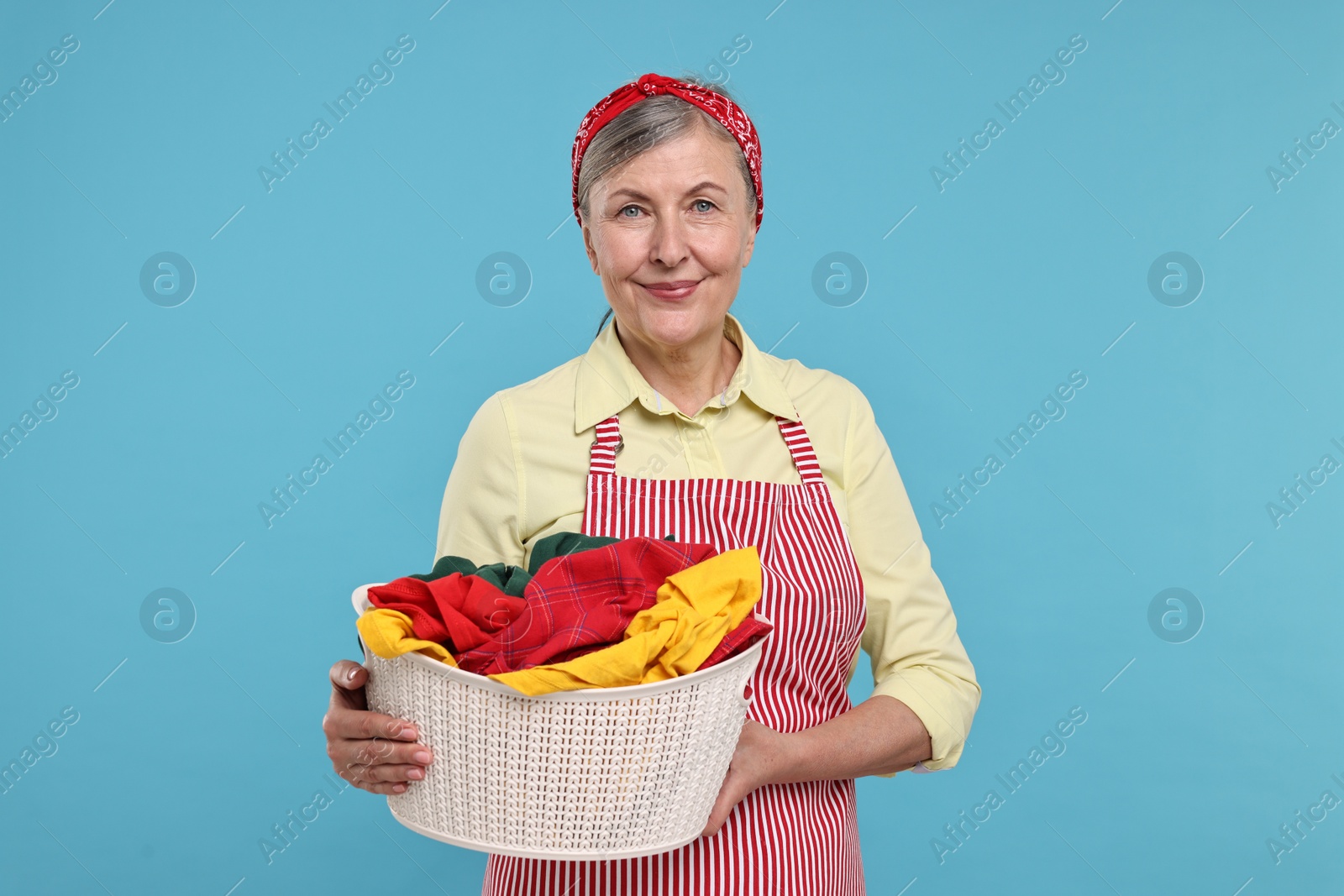 Photo of Happy housewife with basket full of laundry on light blue background