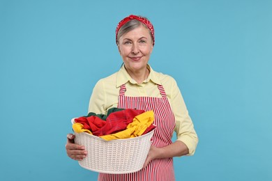 Happy housewife with basket full of laundry on light blue background