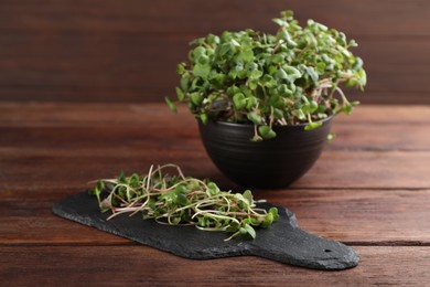 Photo of Bowl and slate board with fresh radish microgreens on wooden table