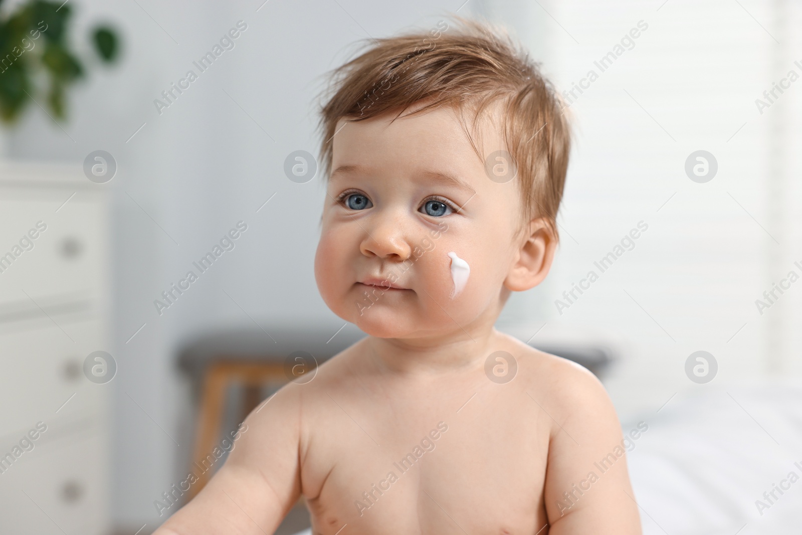 Photo of Cute little baby with moisturizing cream on face indoors
