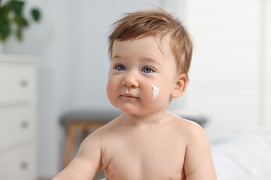 Cute little baby with moisturizing cream on face indoors