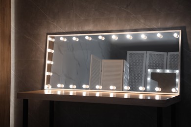 Modern mirror with light bulbs on wooden table in room